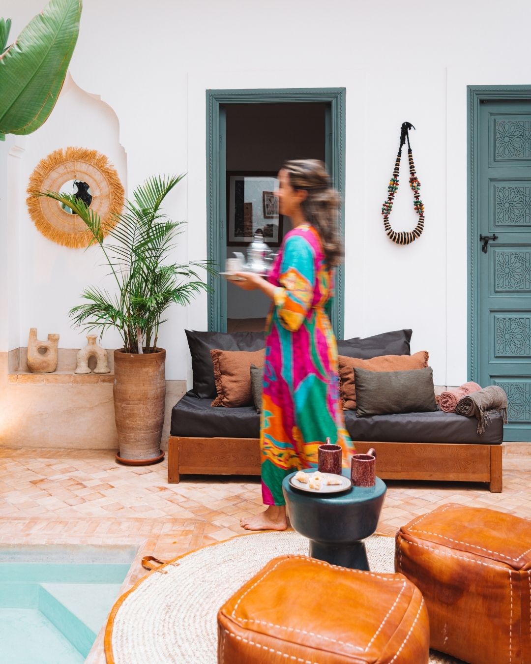 Patio du Riad Melqa à Marrakech : bassin, banquette, poufs en cuir et végétation